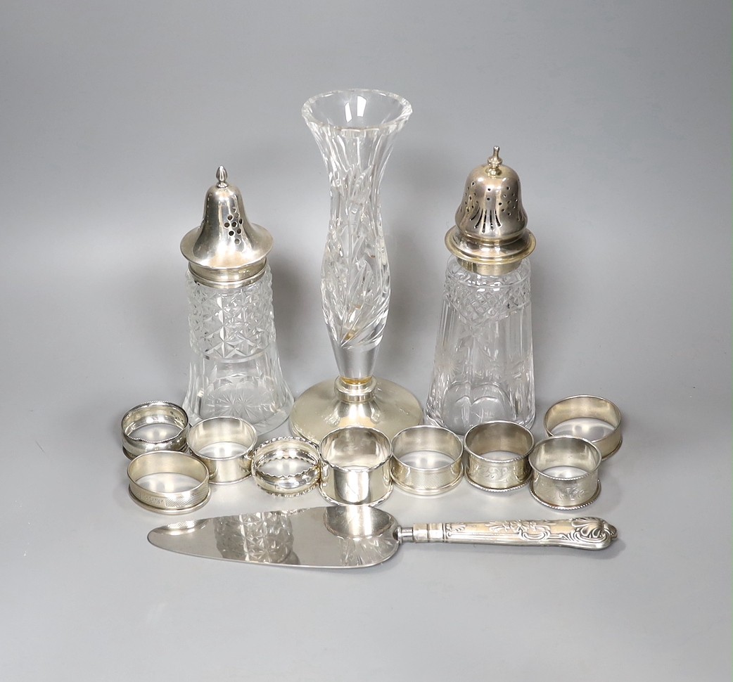 A pair of George V silver napkin rings, Birmingham, 1926, six other silver napkin rings and one stamped 'Silver', a 196's silver handled cake slice, two silver mounted glass sugar sifters and a silver mounted glass posy